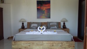 A neatly made bed with a heart-shaped towel arrangement, wooden headboard, and two bedside lamps. - Palm Trees Villas (Gili Air)