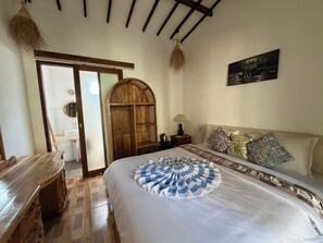 A bedroom with a bed, a wooden wardrobe, a nightstand, a lamp, and a painting on the wall. - Palm Trees Villas (Gili Air)
