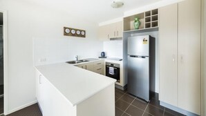 A modern kitchen with white cabinetry, a stainless steel refrigerator, and a built-in oven. - Accommodate Canberra - Century (Griffith)
