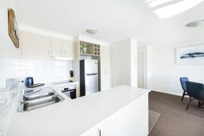 A modern kitchen with white cabinetry, a built-in oven, and a large island with a sink. - Accommodate Canberra - Century (Griffith)