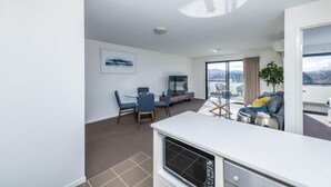 A modern living room with a dining area, a sofa, and a large window offering a view of the outdoors. - Accommodate Canberra - Century (Griffith)