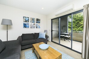 A modern living room with a grey sofa, a wooden coffee table, and a glass door leading to a balcony. - Accommodate Canberra - Domain (Deakin)