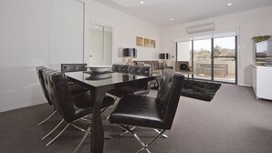 Un espace repas moderne avec une table à plateau en verre, des chaises en cuir noir et une vue sur l’extérieur grâce à de grandes portes coulissantes.