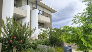 Un immeuble moderne à plusieurs étages, doté de balcons, entouré d’une végétation luxuriante et agrémenté d’un jardin bien entretenu.