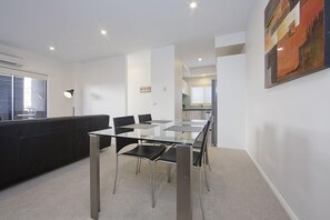 A modern dining area with a glass table and chairs, a black sofa, and a painting on the wall. - Accommodate Canberra - Domain (Deakin)
