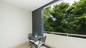 Un balcon avec une table et des chaises, un pot de fleurs et une vue sur des arbres verdoyants.