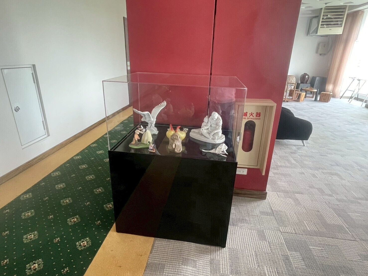 A display of figurines on a black table in a room with patterned carpet and a red cabinet in the background.