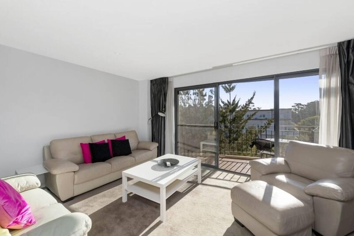 A modern living room with a sofa, a coffee table, and a balcony with a view of the city.