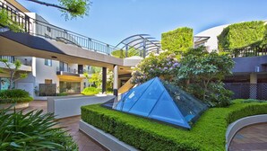 Un bâtiment moderne doté d’une structure pyramidale en verre, entouré d’un espace verdoyant bien entretenu.