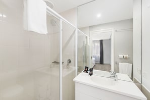 A modern bathroom with a glass shower enclosure, a white vanity with a large mirror, and a visible door leading to another room. - Accommodate Canberra - Griffin (Kingston)