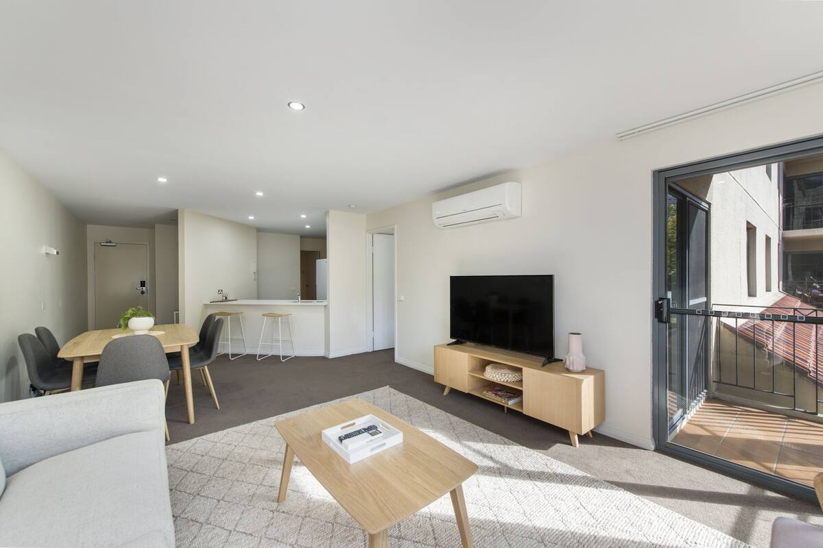 A modern living room with a dining area, a TV, and a sliding glass door to a balcony.