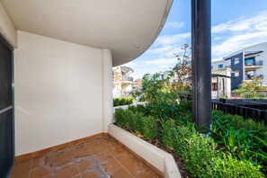 A residential balcony with a tiled floor, a white wall, and a garden area with various plants. - Accommodate Canberra - Griffin (Kingston)