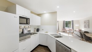Une cuisine moderne avec des armoires blanches, un four à micro-ondes encastré, un four et un lave-vaisselle. L’espace comprend également un coin repas avec une table et des chaises.