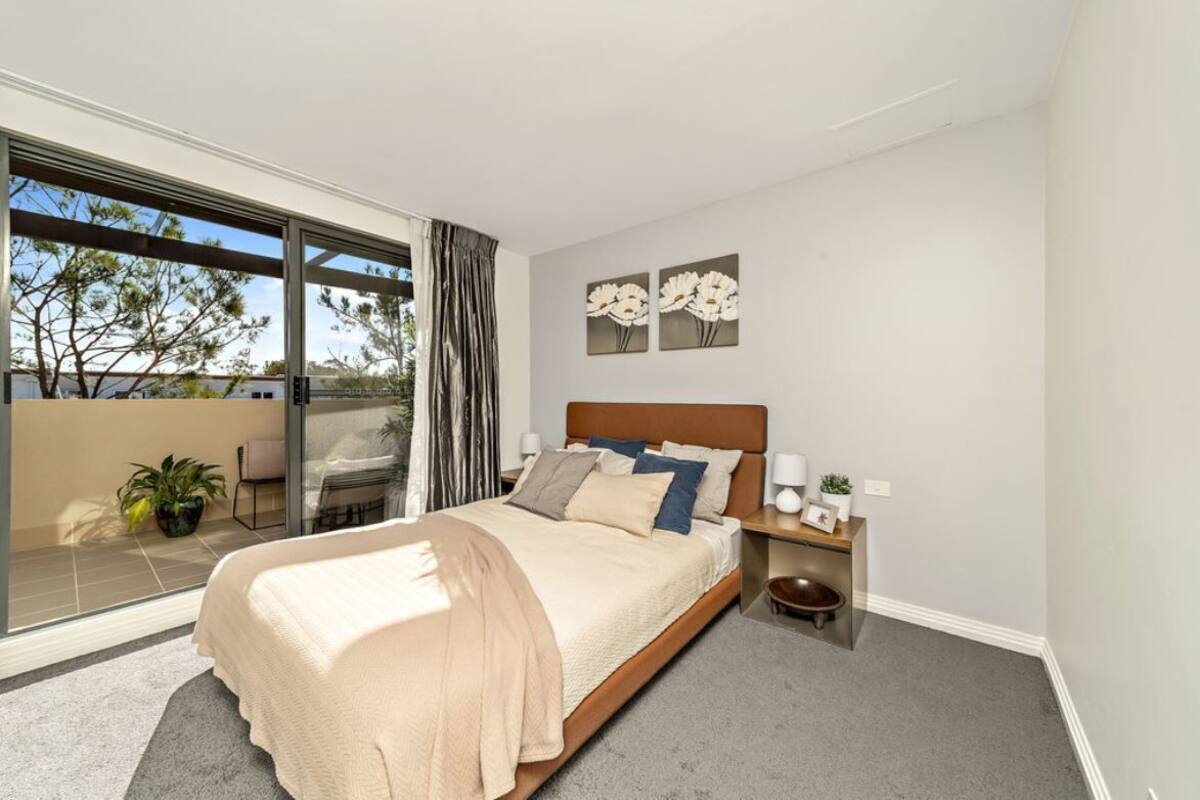 A modern bedroom with a large bed, a nightstand, a potted plant, and a view of the outdoors.
