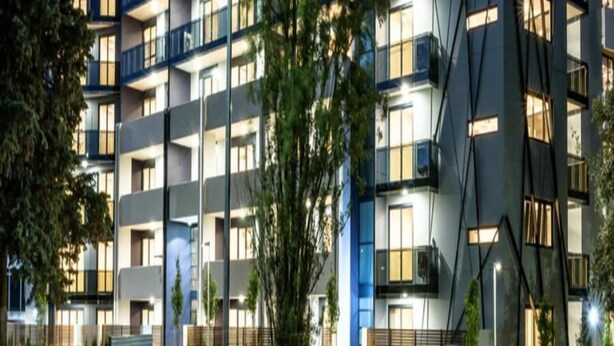 Ein modernes, mehrstöckiges Gebäude mit Balkonen, großen Fenstern und einer gut beleuchteten Fassade.
