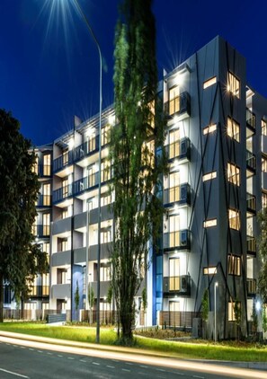 Un immeuble moderne à plusieurs étages, doté de balcons, de grandes fenêtres et d’une façade bien éclairée.