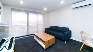 Ein modernes Wohnzimmer mit einem dunkelblauen Sofa, einem Holztisch, einem hellen Holzstuhl und einem großen Fenster mit Blick.