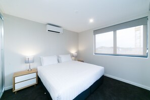 A modern hotel room with a large bed, bedside tables with lamps, an air conditioning unit, and a large window with a city view.