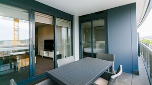 Ein Balkon mit Tisch und Stühlen, eine Schiebetür zu einem Zimmer und Blick ins Freie.