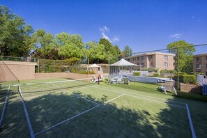Una cancha de tenis con red, rodeada por una valla y árboles.