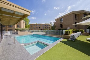 Una piscina rectangular con borde de baldosas, rodeada por una valla blanca y follaje.