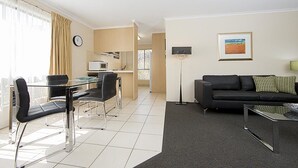 Ein modernes Wohnzimmer mit einer schwarzen Couch, einem Glastisch und einem Essbereich mit Tisch und Stühlen.