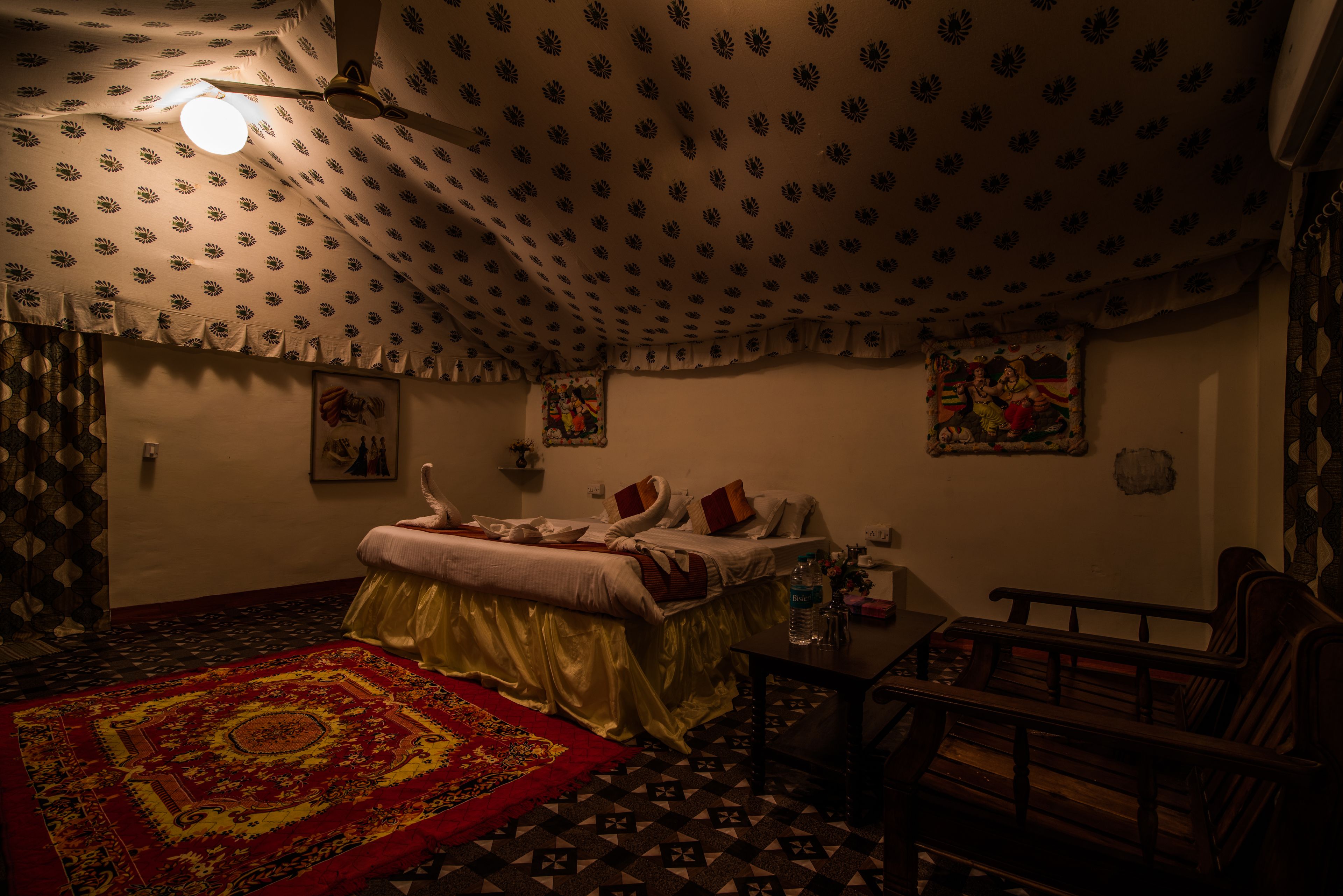A room with a patterned ceiling, a bed with pillows, a wooden bench, and a red patterned rug.