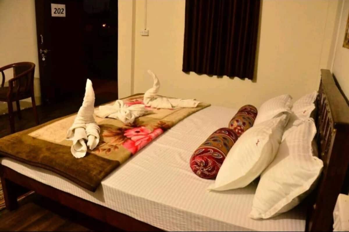 A hotel room with a bed, a chair, a door with a number, and a window with curtains.