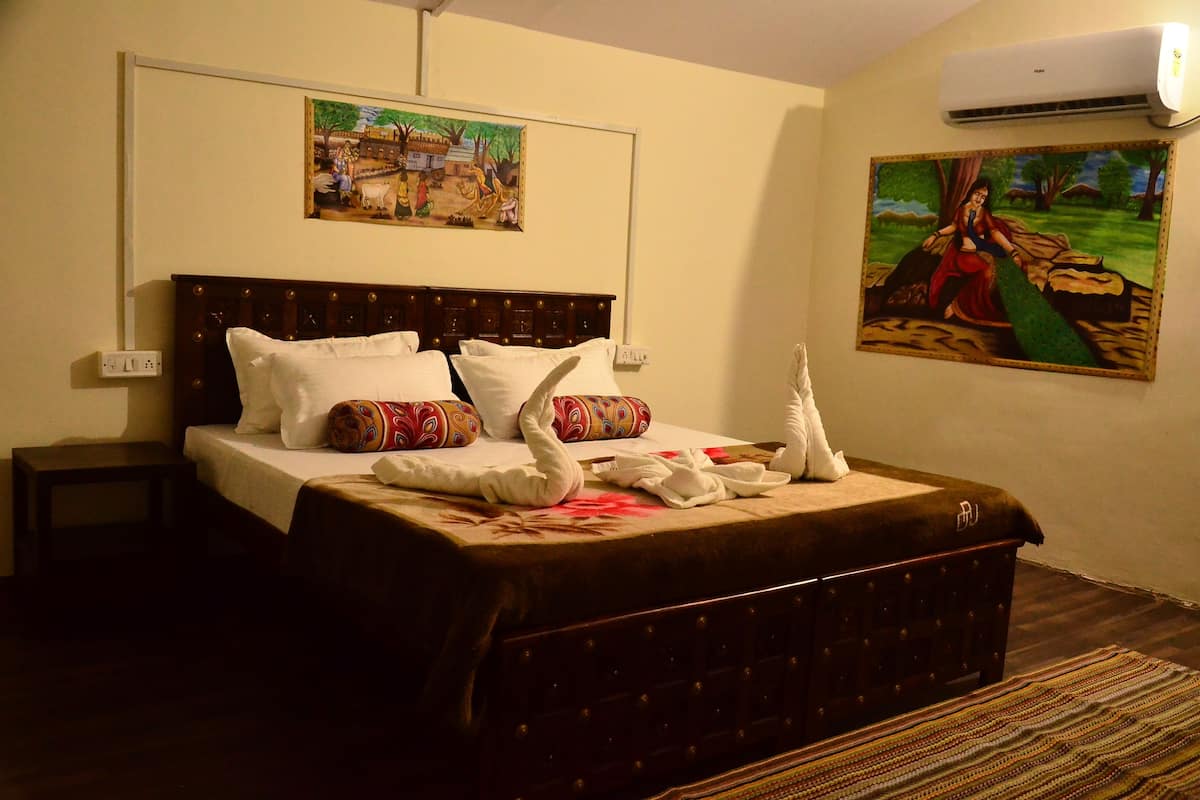 A bedroom with a large bed, a headboard, a bedside table, and two wall-mounted paintings.
