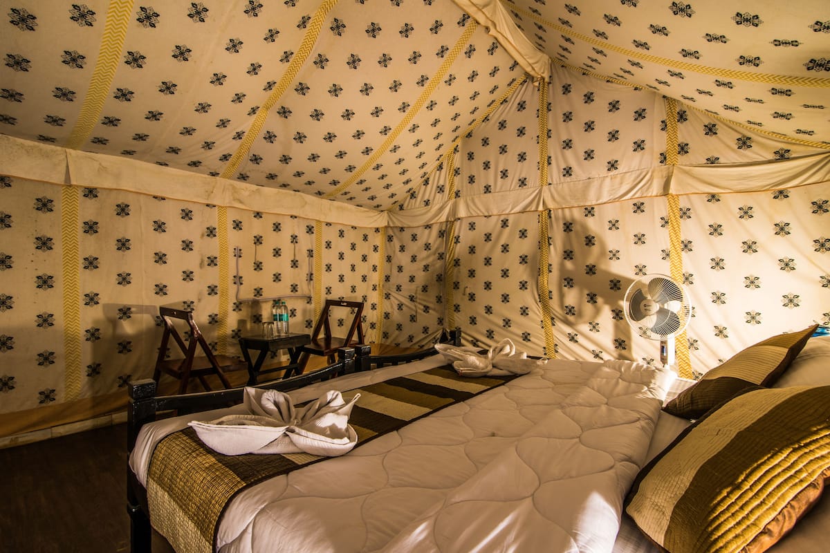 A tent-style room with a bed, a fan, and a table with chairs.