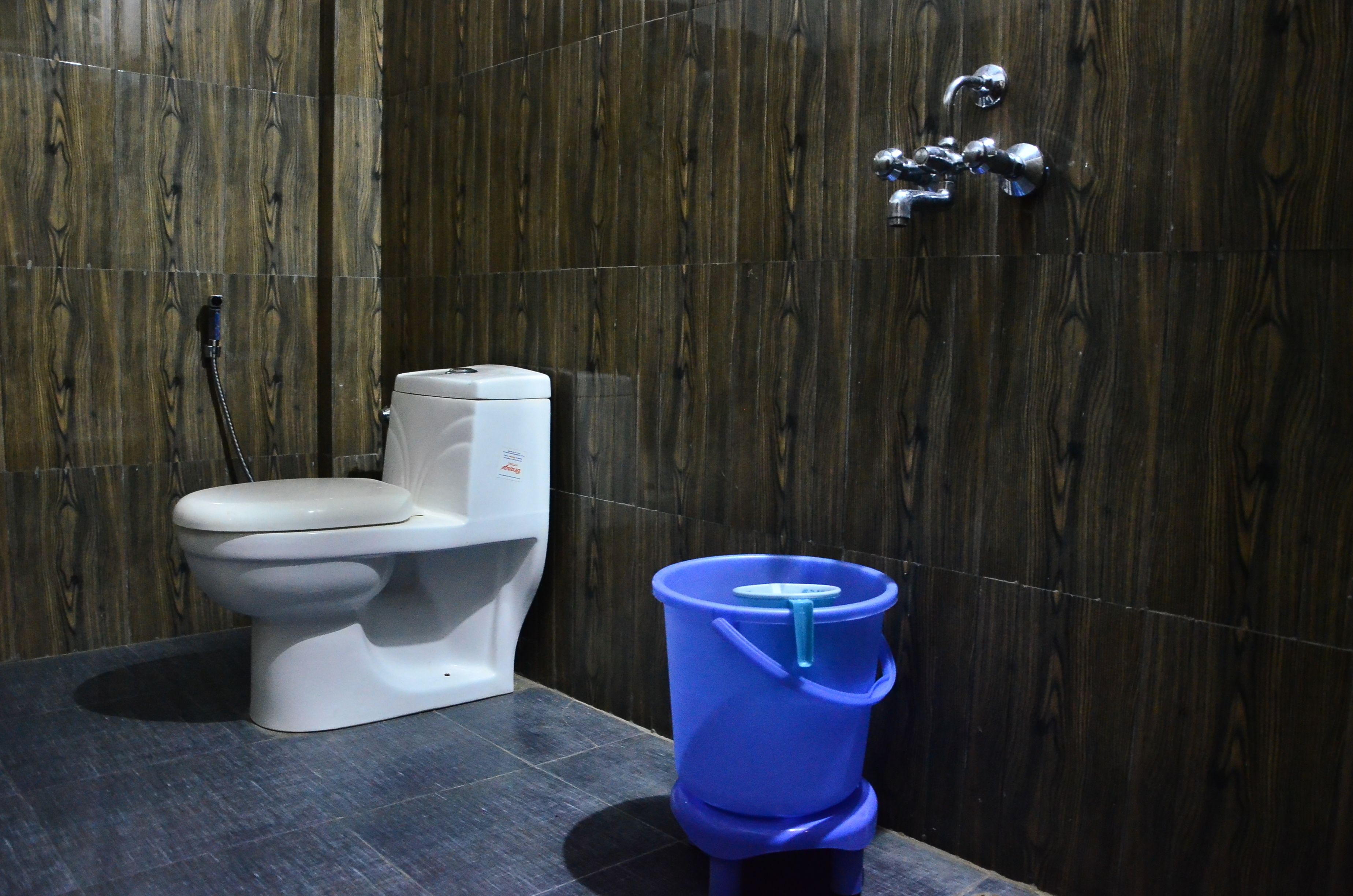 Un bagno moderno con una parete in legno, un water bianco e un secchio blu.