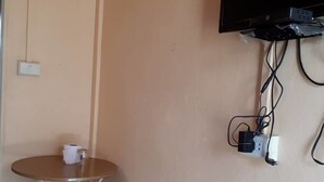 A small room with a television mounted on the wall, a power outlet, and a table with a chair. - Aranya Resort (Prakhon Chai)