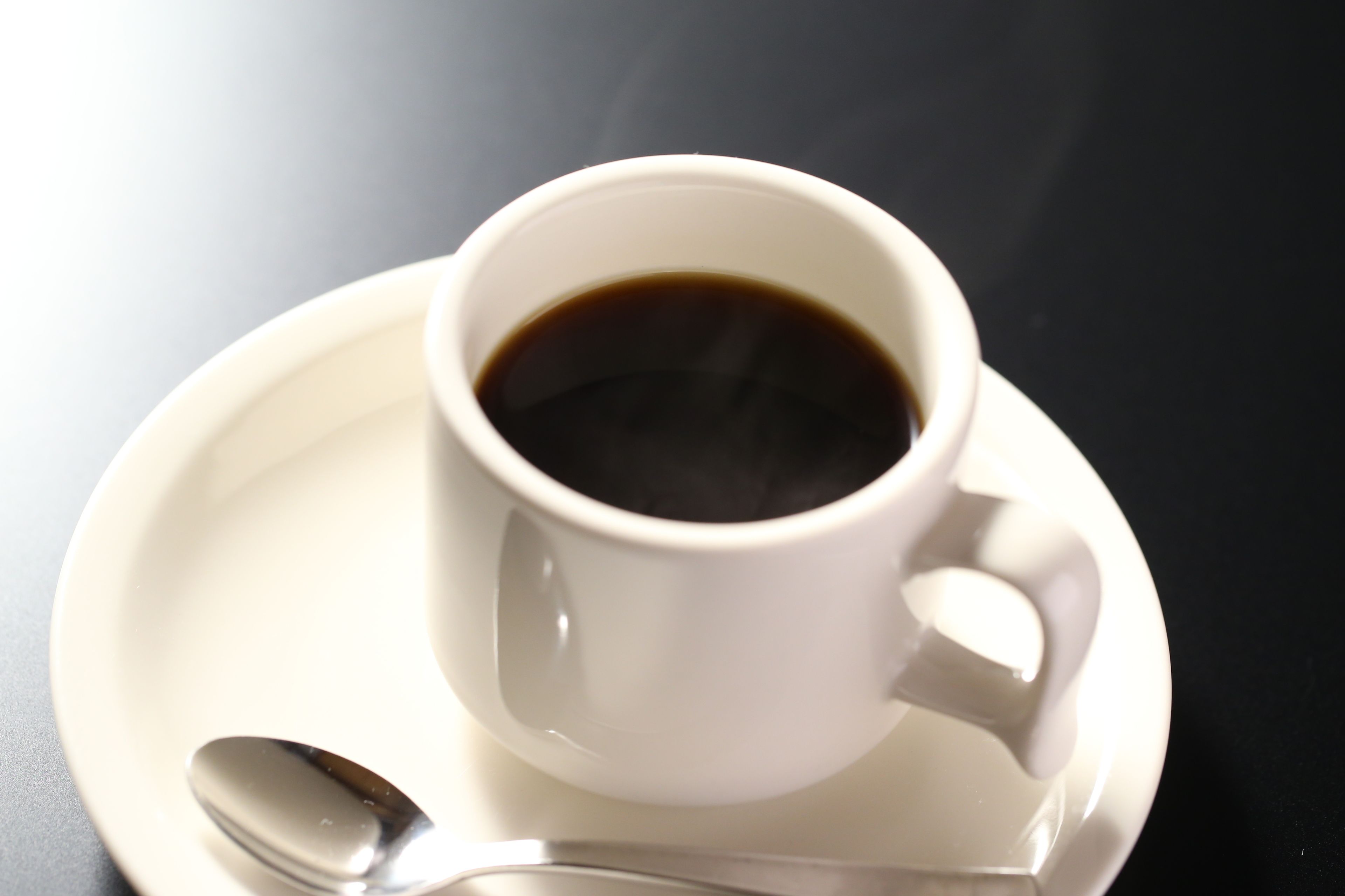Una taza blanca de café sobre un plato con una cuchara al lado.