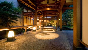A covered outdoor area with wooden beams, lanterns, and a gravel path leading to a traditional Japanese garden. - Club Wyndham Chikumakan Nagano (Chikuma)