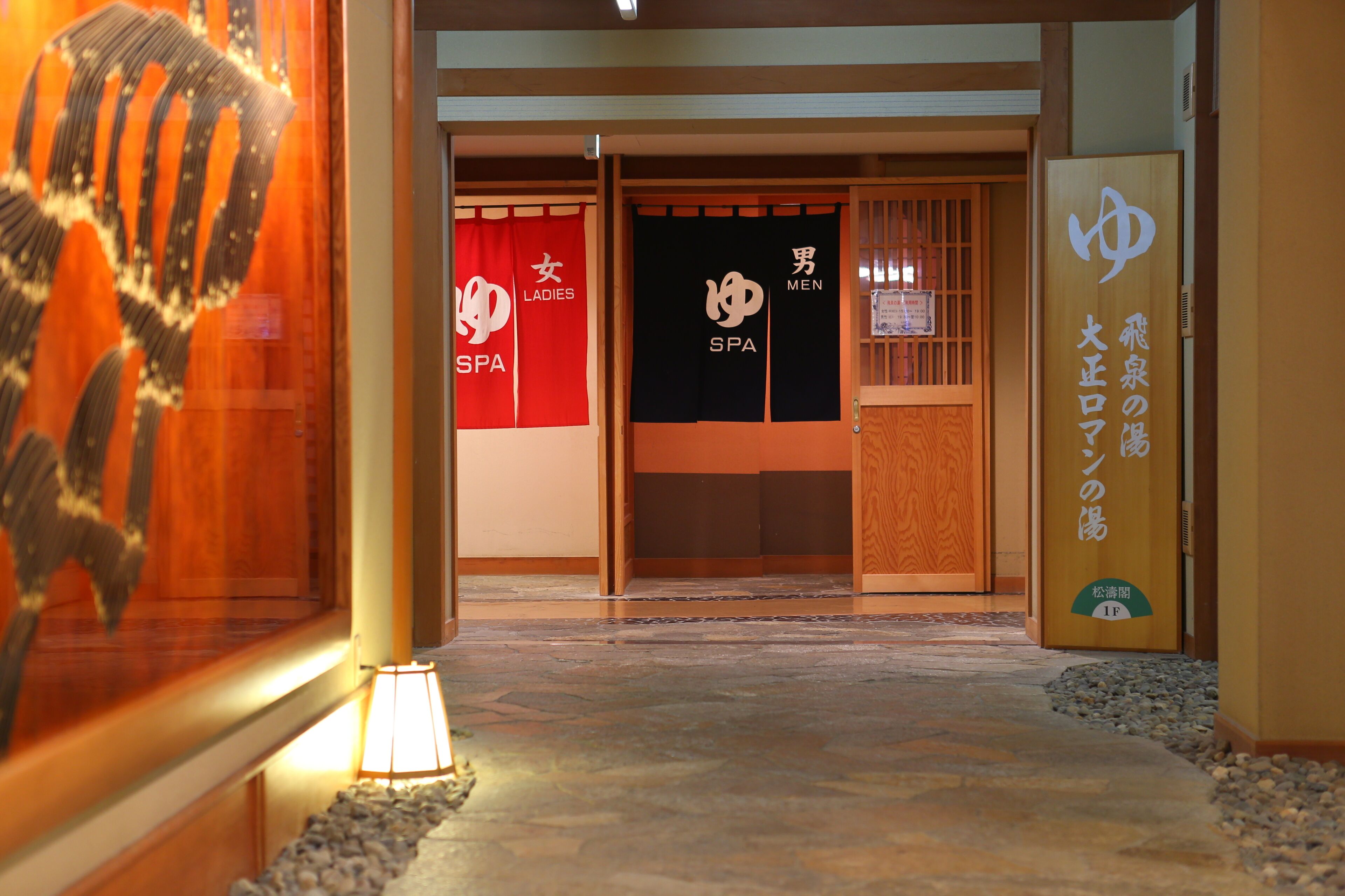 Entrada de un spa japonés tradicional con puertas separadas para señoras y caballeros, suelo de madera y un letrero que indica el nombre del spa.