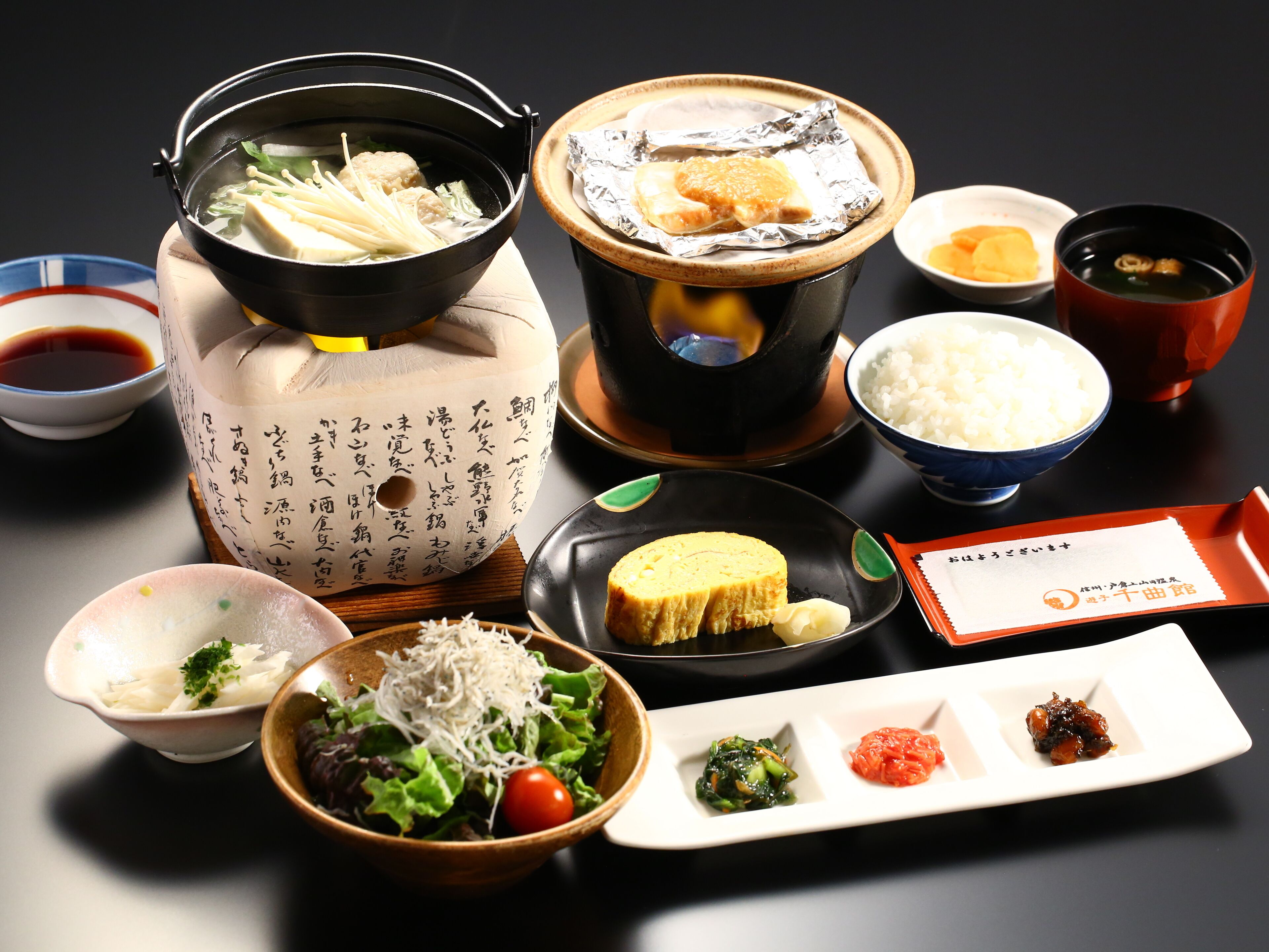 Diversos pratos japoneses, incluindo um fondue, arroz, salada e pequenas porções de picles e molhos.