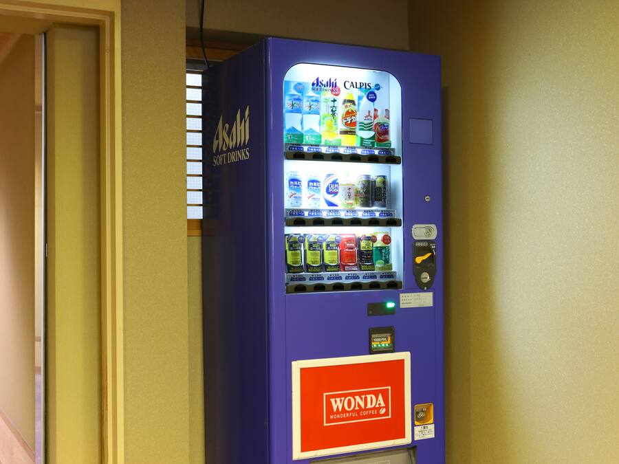 A vending machine with multiple drink options, including Asahi soft drinks and Wonda coffee, located in a hallway.