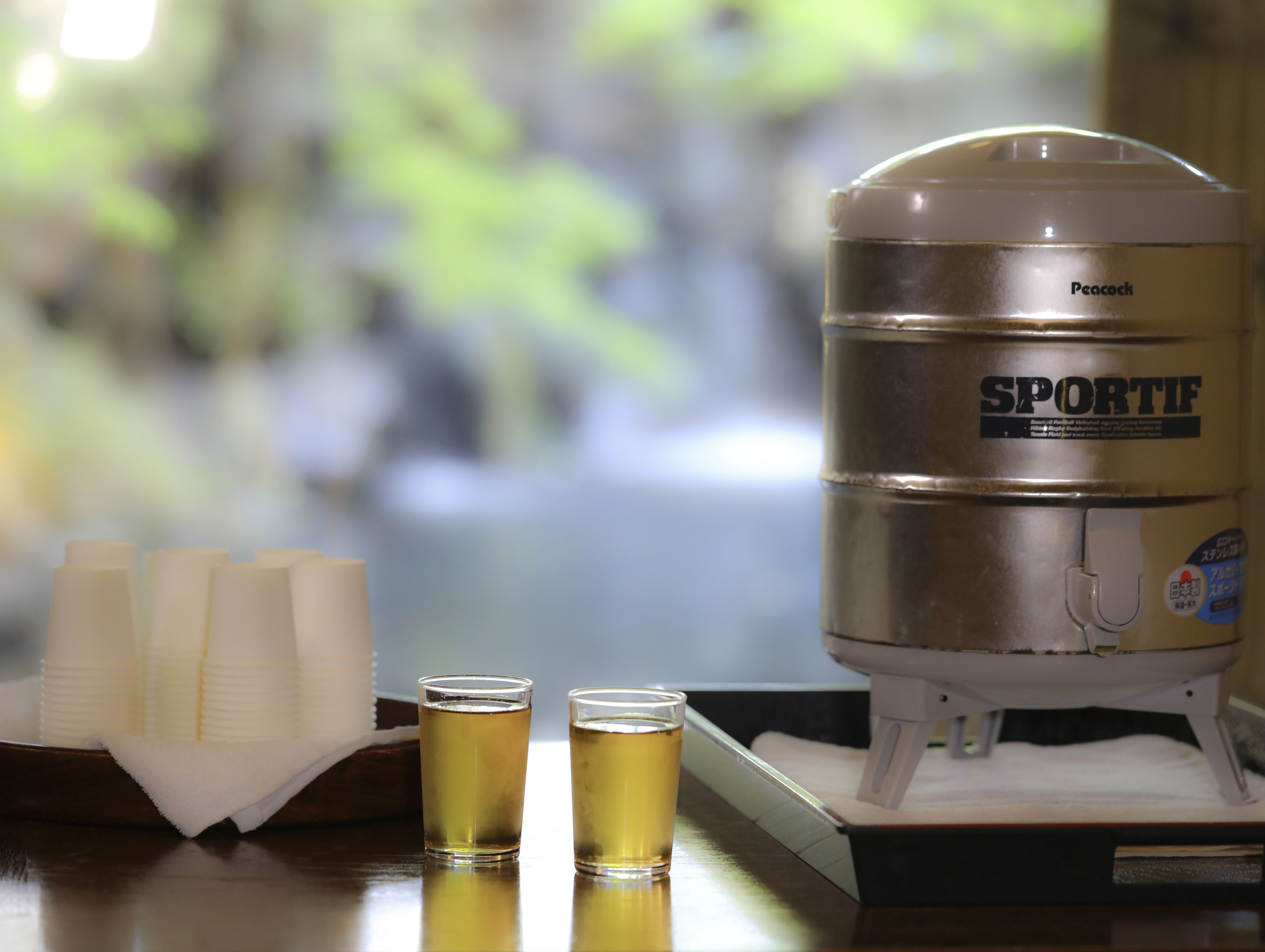 Un dispensador de agua Peacock SPORTIF con dos vasos de agua sobre una mesa.