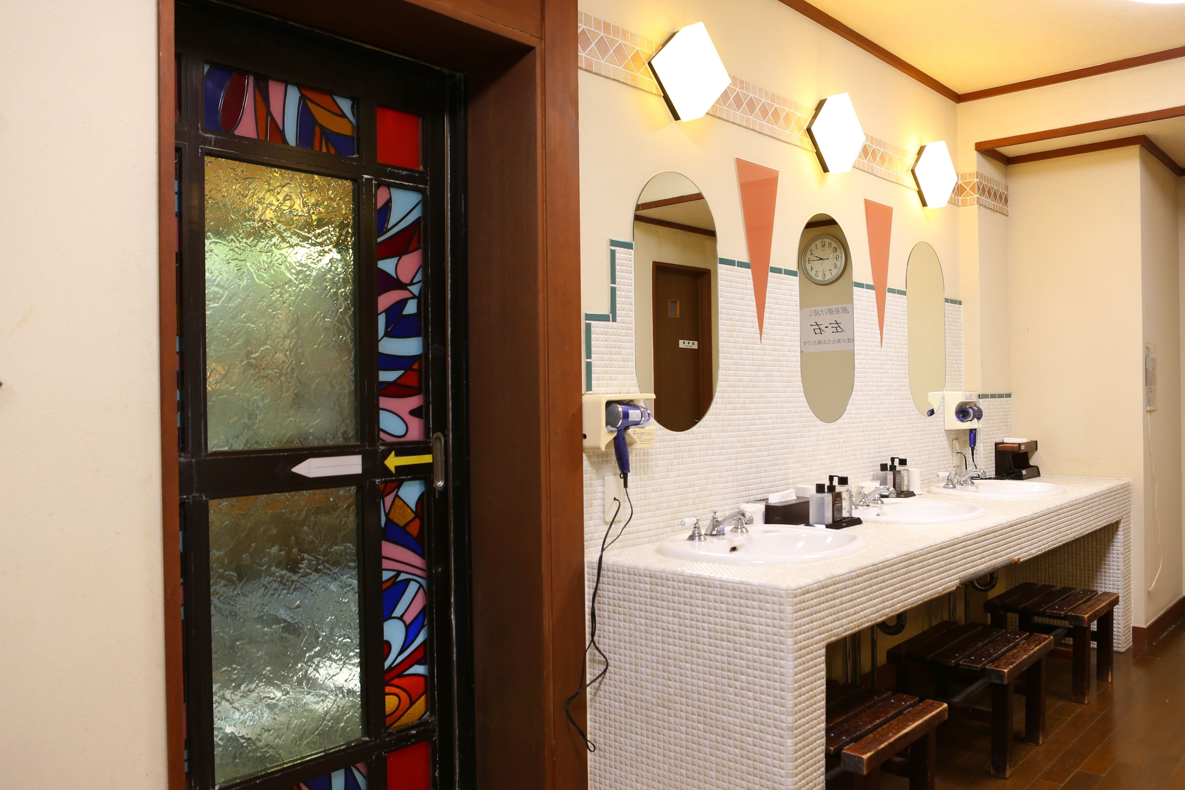 Un baño con un espejo grande, dos lavamanos y bancos.