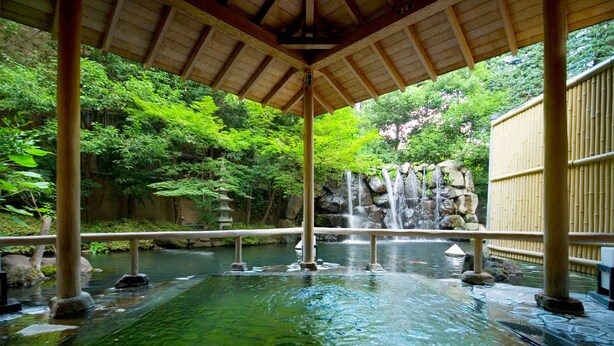 A traditional Japanese onsen with a wooden roof, a rock waterfall, and a bamboo fence. - Club Wyndham Chikumakan Nagano (Chikuma)