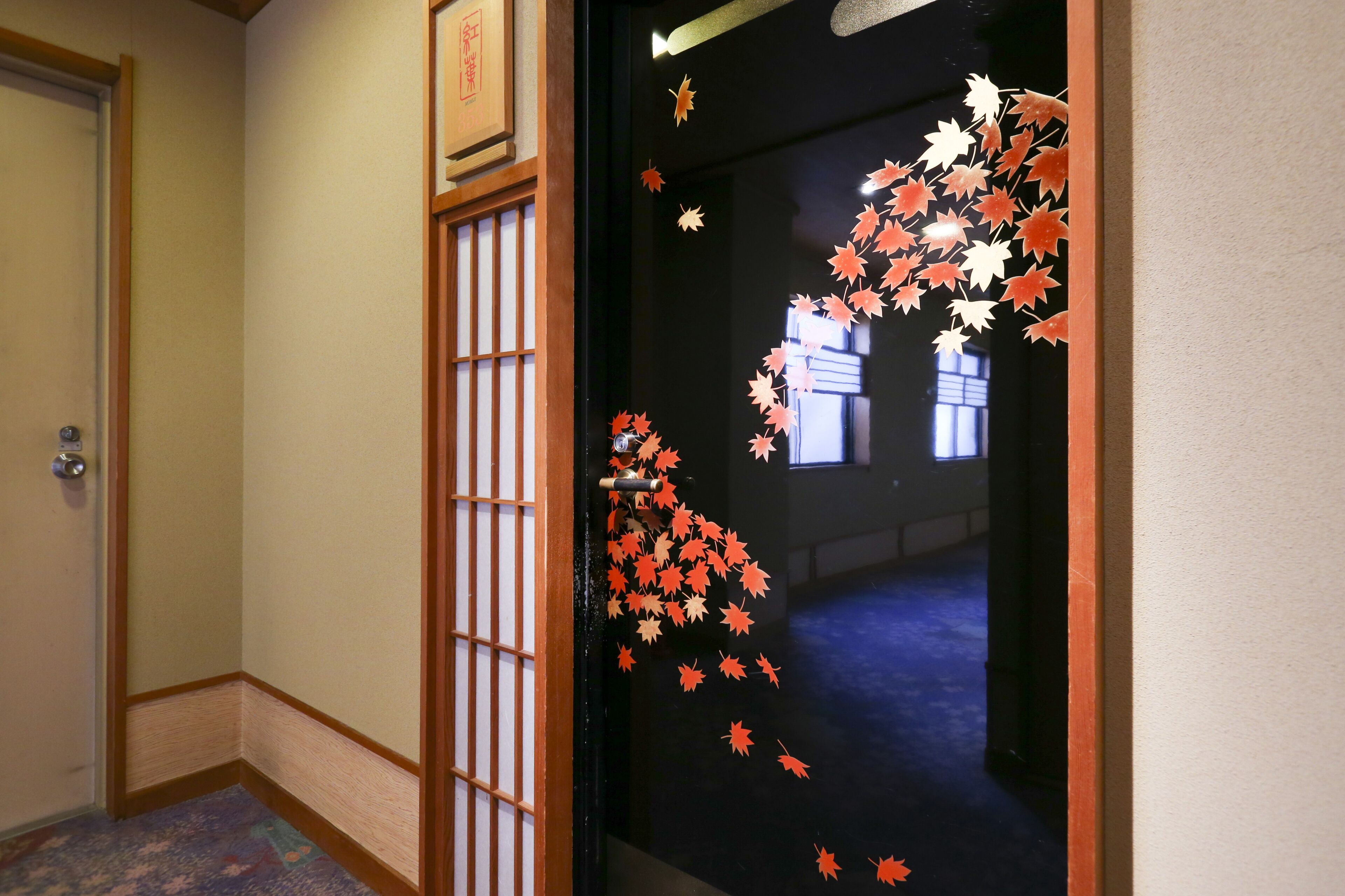 A hallway with a traditional Japanese-style door, a wooden floor, and a view into another room.