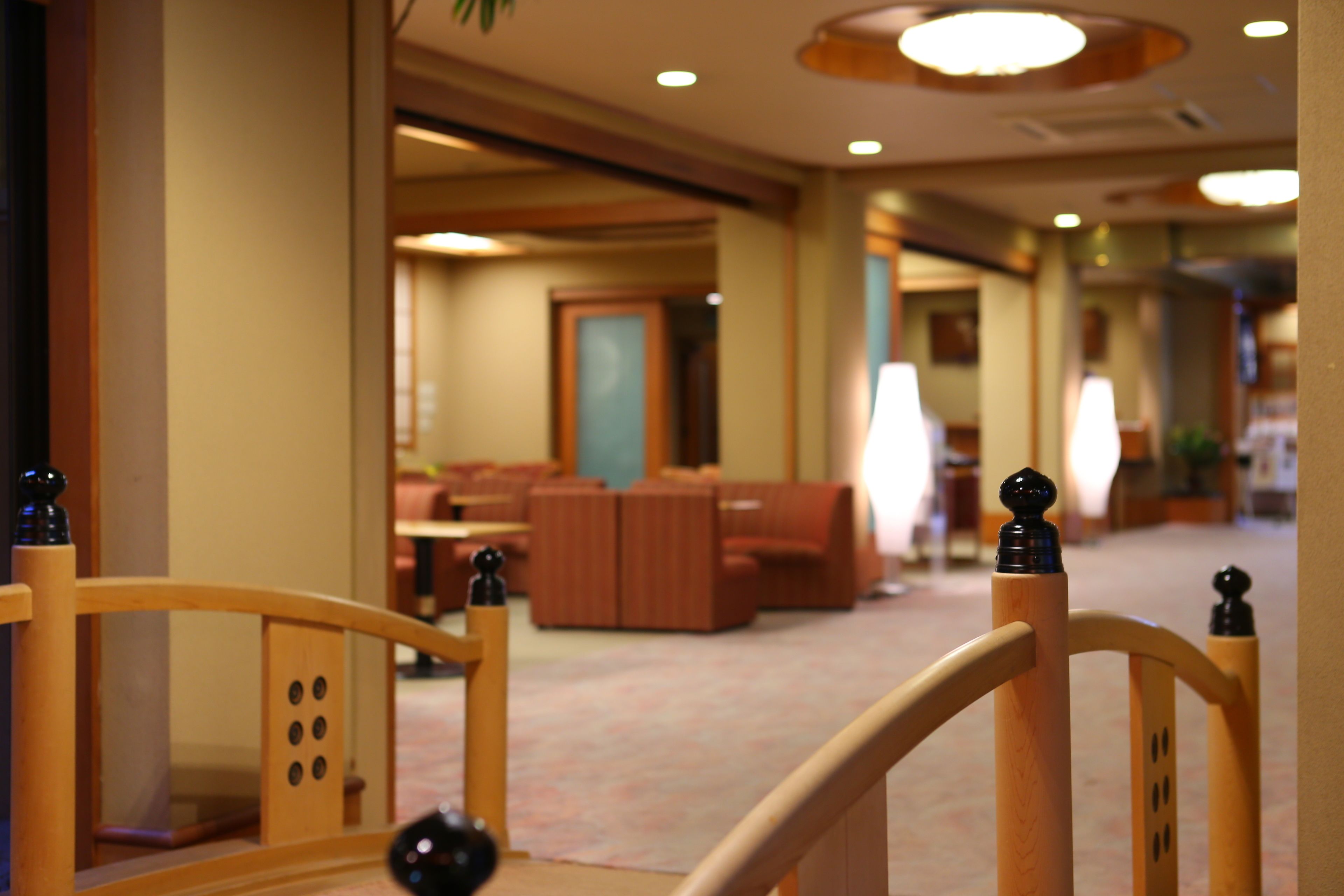 A hotel corridor with a wooden railing, a seating area with sofas, and a door in the background.