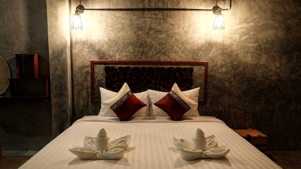 A neatly made bed with a striped bedspread, two decorative pillows, and two towels arranged in a bow shape. - Sirah Hometel - Hostel (Ko Pha-ngan)