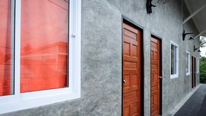 A building with a grey textured exterior, large windows with white frames, and wooden doors with numbers. - Sirah Hometel - Hostel (Ko Pha-ngan)