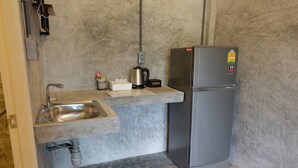A compact kitchenette with a stainless steel sink, a kettle, and a refrigerator. - Sirah Hometel - Hostel (Ko Pha-ngan)