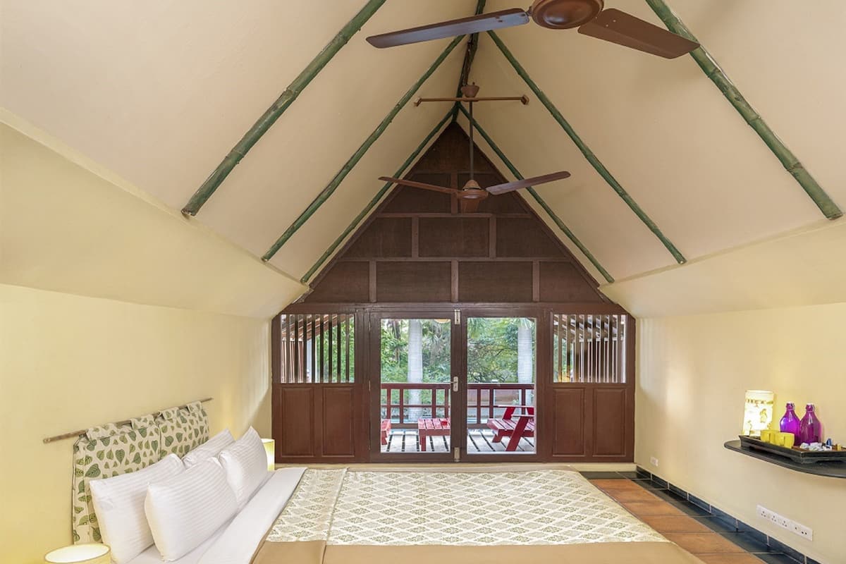 A bedroom with a bed, a ceiling fan, a window with a view of the outside, and a shelf with items on the wall.