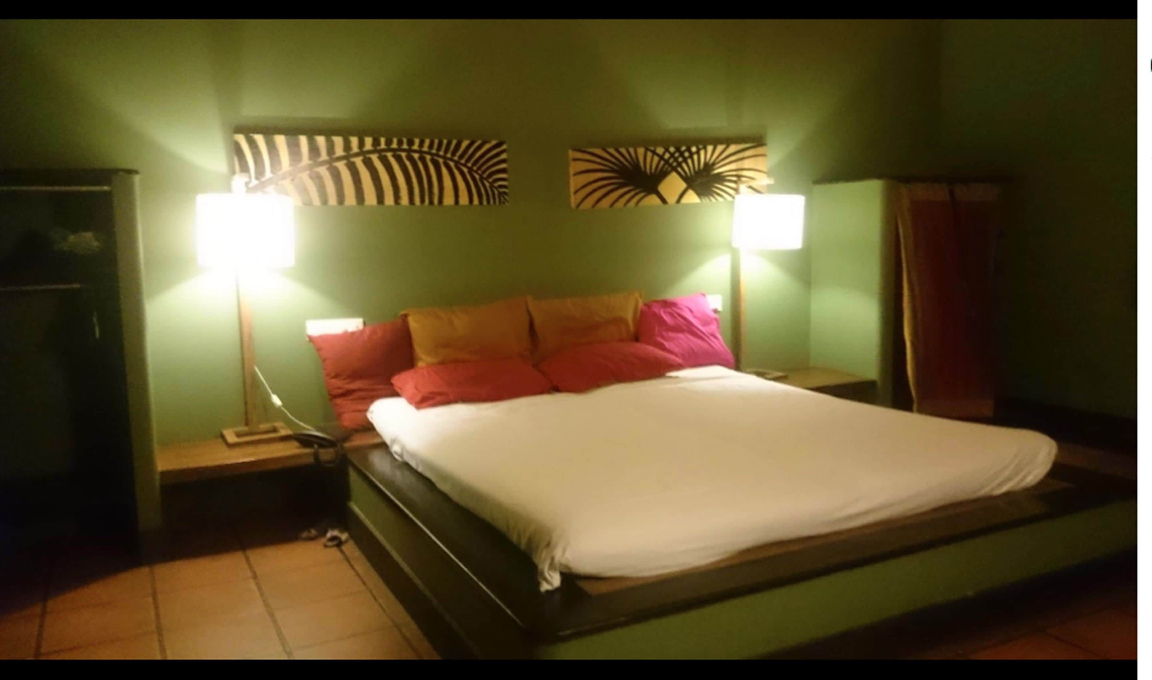 Habitación individual con una pared verde, dos lámparas de noche y un cabecero estampado.