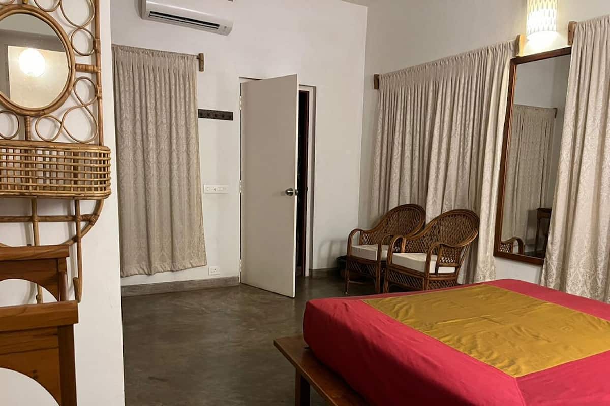 A hotel room with a bed, two chairs, a mirror, and a door.
