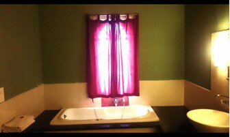 Un baño con bañera, lavamanos y ventana con cortinas rosas.