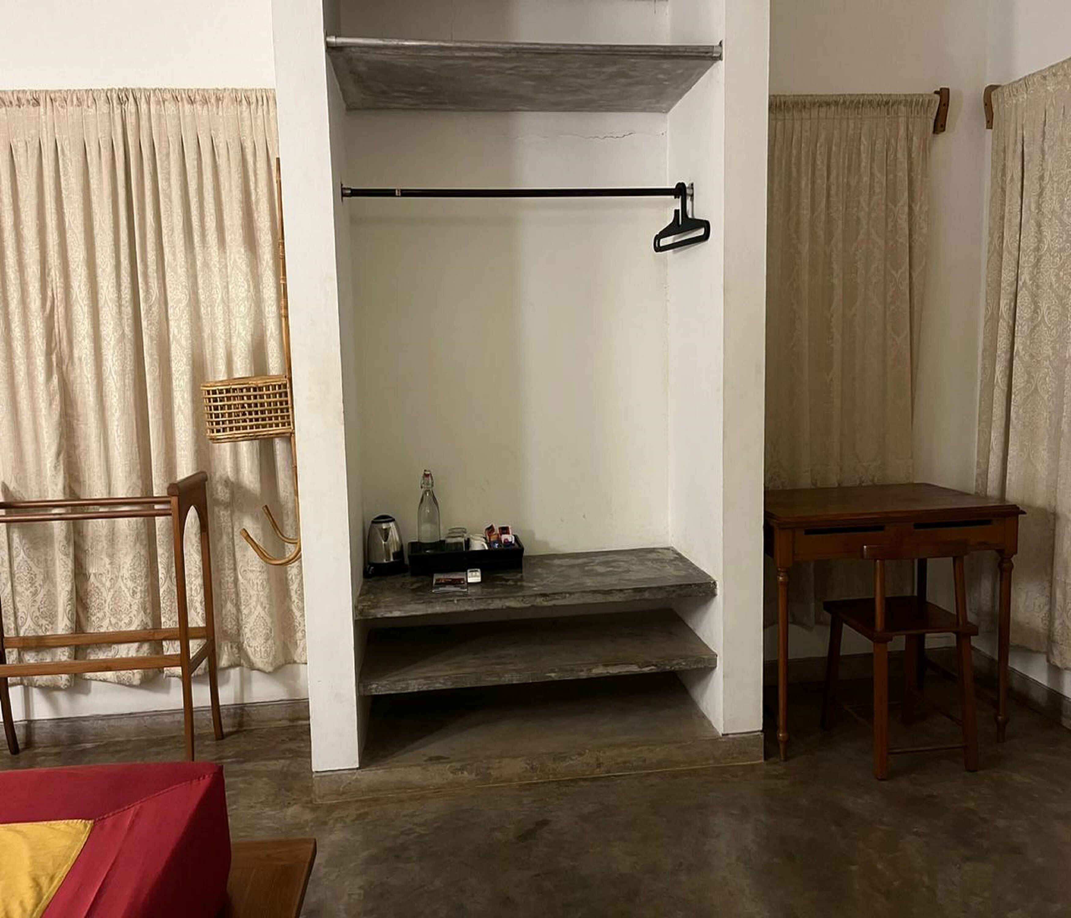 A room with a wooden chair, a small table, a shelf with a bottle and a tray, and a hanging coat rack.